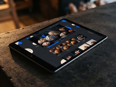 Angled mockup of a modern local bakery website displayed on a sleek tablet, warm side-lighting casting soft shadows on a dark concrete surface.