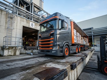 Low-angle heroic shot of a modern orange and charcoal cargo truck at a concrete loading dock, crisp morning daylight, industrial atmosphere