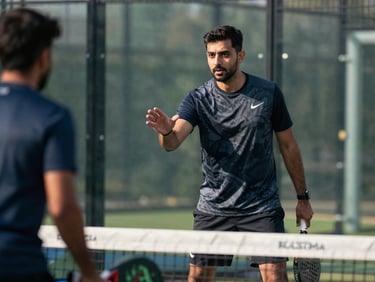 Coach Sikandar Hayat court-side on a padel court, mid-instruction gesture toward a player in natural daylight, authoritative stance, no posed look toward camera
