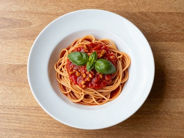 Overhead shot of a white bowl of pasta with a rich tomato sauce and fresh basil leaves on top, natural daylight, ceramic bowl on a clean wooden table