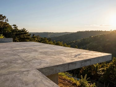 Wide-angle architectural photograph of a raw concrete cantilevered terrace projecting over a forested valley during the low-sun golden hour, dramatic shadows.