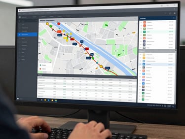 Close-up of a logistics operations dashboard on a large monitor, showing live shipment map with route lines, delivery status columns, and freight data tables, hands resting at keyboard in foreground, clean dark-themed interface