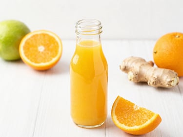 A glass bottle filled with bright orange citrus juice, with fresh sliced oranges and ginger root on a clean white background, soft daylight