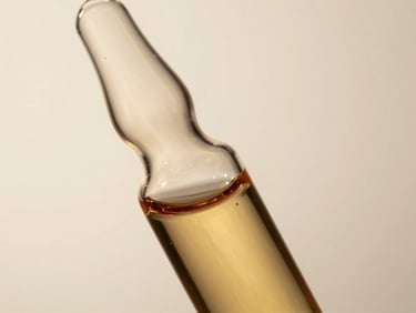Close-up of clear amber liquid in a minimalist glass vial, soft studio light, warm neutral background