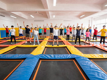 Wide environmental shot of a large school group posing together on wall-to-wall trampolines, bright indoor lighting, energetic atmosphere