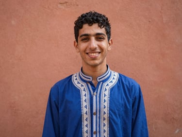 صورة لوجه شاب مغربي بابتسامة دافئة، يرتدي قميصًا تقليديًا، إضاءة طبيعية ناعمة، 35mm