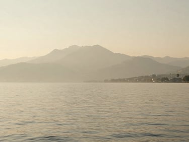 A quiet afternoon on Lake Geneva, soft light reflecting on the calm water, distant mountains in a hazy warm beige mist, minimalist composition.