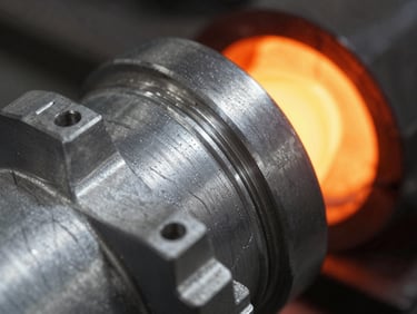 High-contrast macro photograph of a complex cast aluminum component with visible parting lines, sharp technical details, deep shadows, warm orange glow from molten metal in the background, 50mm lens
