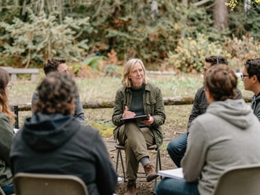 Washington community leader facilitating a small group discussion outdoors, natural Pacific Northwest daylight, soft earthy tones, candid interaction, 35mm lens.