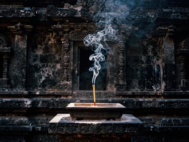 Delicate plumes of white incense smoke rising in a sharp shaft of light against a dark, carved stone temple wall, 35mm film.