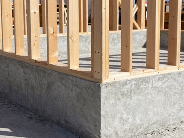 Close-up of freshly poured concrete foundation and pristine structural timber framing under bright daylight