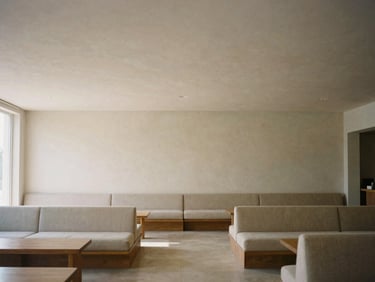 Wide environmental shot of a minimalist lounge area, high ceilings, clean architectural sightlines, warm neutral earth tones, diffused natural daylight.