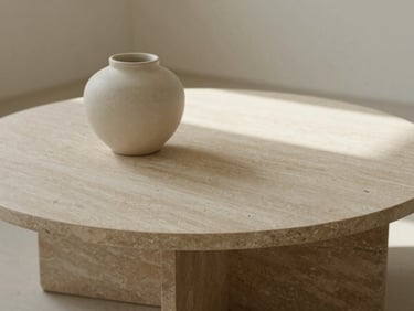 Detail crop of a raw travertine coffee table with a single ceramic vessel, warm morning light, soft shadows, minimalist interior design.
