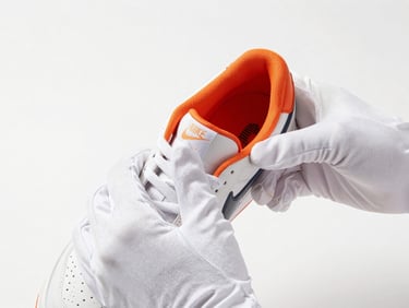 Close-up of hands wearing white gloves carefully handling a rare, limited-edition sneaker, clean white background, crisp studio lighting, focus on intricate stitching and unique material texture