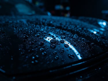 Dark high-contrast automotive photography, macro shot of water beading on a freshly waxed black sports car hood under neon blue lights, sharp reflections, 35mm lens
