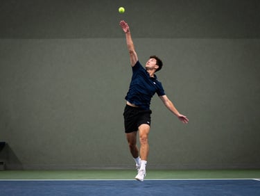 An adult player mid-air executing a focused serve on an indoor court, crisp illumination