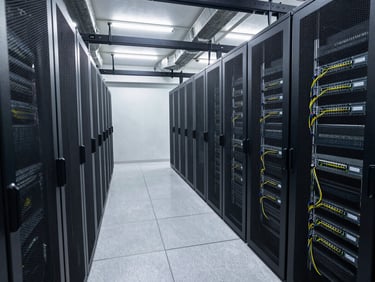 Wide shot of a data center floor — rows of server racks with visible PDU cable management and overhead cooling ducts, cool white lighting rendering equipment labels sharply, no people present
