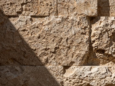 Close-up of a rough-cut limestone facade detail in Amman, natural north-facing light raking across the stone surface revealing texture and coursing, tight architectural framing, no people
