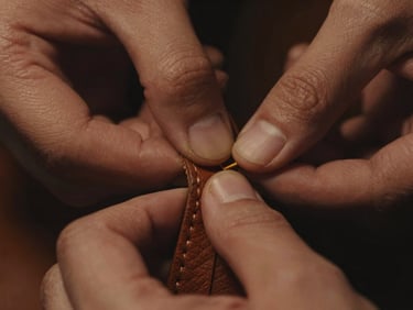 Extreme close-up of textured leather being stitched, hands in low light, sharp focus on the thread, warm tones