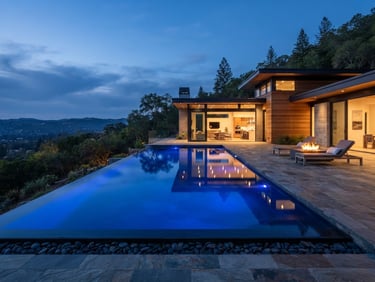 Architectural photography of a perimeter-overflow concrete pool at twilight, glowing deep blue water reflecting modern home lines, natural slate hardscaping, wide-angle environmental frame