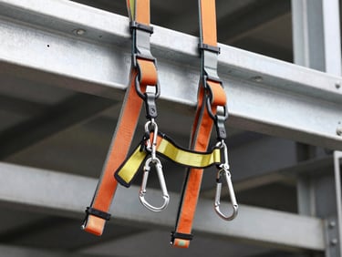 Industrial safety harness with heavy-duty carabiners and lanyards, mounted on a steel beam, high-contrast, technical detail.
