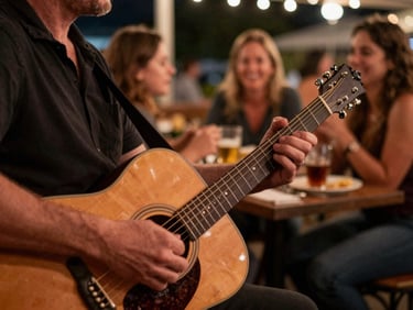 Close-up of a musician hands playing an acoustic guitar on an outdoor stage at night, warm copper lighting, soft focus background of happy diners