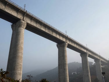 Low-angle heroic shot of a heavy concrete railway bridge crossing a valley, early morning mist, high-contrast industrial composition