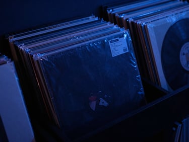 Moody close-up of vinyl record sleeves stacked in a dark room under soft blue lighting