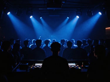 Moody wide shot of a DJ booth in a dark club, silhouettes of the crowd dancing under deep indigo and cobalt spotlights, high contrast, atmospheric 35mm film grain