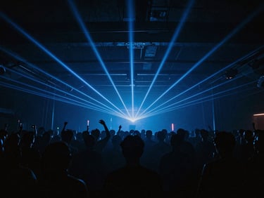 Wide panoramic shot of a dark industrial venue, blue laser beams cutting through haze, crowd silhouettes