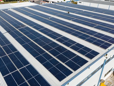 Wide-angle technical aerial view of a massive industrial warehouse roof covered in solar panels, bright daylight, high contrast blue and slate tones, sharp drone perspective