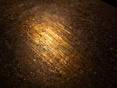 Abstract texture of brushed gold leaf on dark stone, low-key warm golden lighting, shallow depth of field, 50mm lens