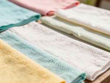 Close-up of colorful artisanal fabrics with delicate hand-stitching details, warm natural daylight, shallow depth of field