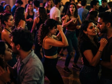 A crowded dance floor at night, dramatic low-light with rich ambient colors, natural motion blur, people dancing with uninhibited joy, 35mm film grain