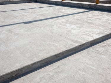 Wide-angle architectural shot of a finished commercial concrete foundation slab in Birmingham, harsh midday sun casting deep geometric shadows on the textured concrete, 35mm.
