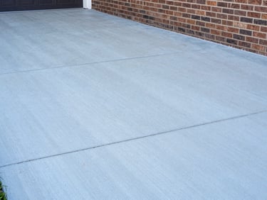 Close-up of clean concrete driveway next to brick siding, showing sharp contrast between washed and unwashed areas, bright daylight, sharp focus, 35mm