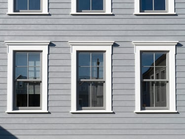 Straight-on architectural shot of a freshly painted gray residential exterior, clean white window frames, bright daylight, sharp focus, 35mm