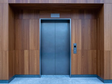 Modern residential elevator lobby with warm wood paneling and a clean, minimalist elevator door in cool grey steel