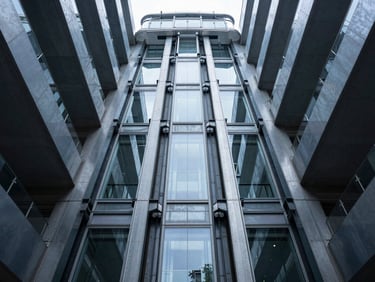 Low-angle symmetrical architectural photograph of a sleek glass elevator shaft rising through a modern steel atrium, cool daylight, high-contrast steel textures.