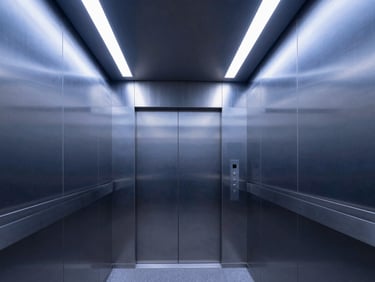 Sleek commercial elevator interior with brushed steel panels, minimalist mirror accents, and cool architectural LED lighting