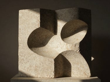 Escultura abstracta de piedra con formas geométricas, luz lateral creando sombras dramáticas, textura rugosa.