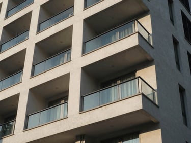 Exterior view of a premium modern apartment building in Kathmandu, showing balconies catching bright afternoon sun and clean glass railings.