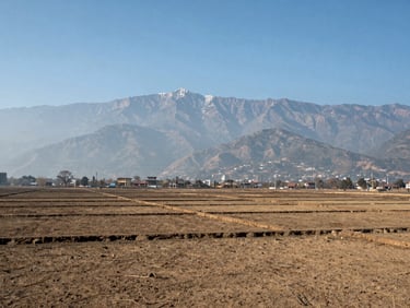 Scenic wide-angle shot of a flat plotting land in Pokhara, showing clear physical boundaries with a mountain backdrop under clear blue sky.