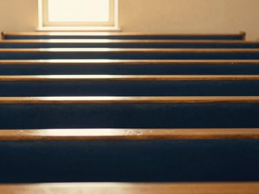 A warm, light-filled sanctuary with soft gold accents, empty wooden pews, light streaming through a window