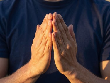 Two people with hands gently folded in prayer, soft golden-hour light, warm and compassionate atmosphere