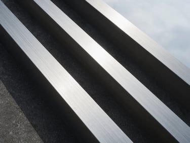 Abstract close-up texture of brushed silver steel and dark concrete, sharp architectural lines, cool overcast daylight, deep controlled shadows.