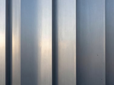 Abstract texture of brushed silver metal panels reflecting cool, diffused daylight, architectural detail