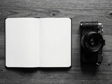 Stark monochrome flat-lay of an open notebook and a camera on a wooden table, sharp focus, 35mm