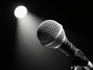 Stark high-contrast desaturated close-up of a microphone on a dark stage, spotlight beam, deep blacks, crisp whites