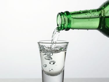 Close-up macro shot of a condensation-beaded green Chamisul bottle, clean pour into a traditional shot glass, high-key studio lighting, cool emerald tones.